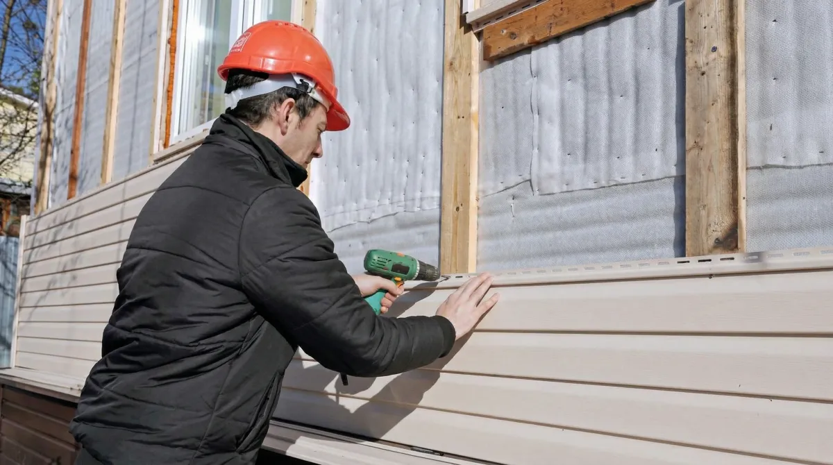 Siding replacement professional using a power drill to install new tan vinyl siding on a home exterior in Savannah, GA